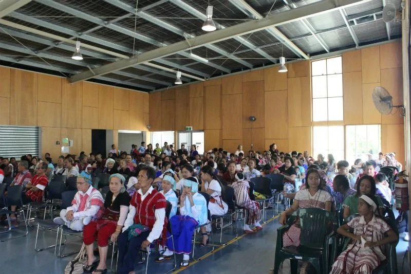 A hall full of people seated for the Karen New Year celebration in Brisbane, many in traditional Karen dress.